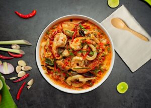 Resep Tom Yum Thailand: Sup Asam Pedas yang Kaya Rempah Semangkuk tom yum seafood pedas khas Thailand dengan rempah segar, disajikan di atas meja gelap bersama sendok kayu.