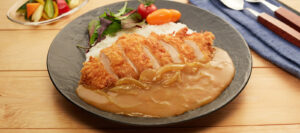 Sepiring chicken katsu curry Jepang berisi nasi putih, potongan ayam goreng tepung renyah, kuah kari kental dengan irisan bawang bombay, serta sayuran segar sebagai pelengkap.
