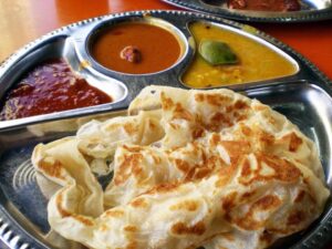 Roti canai tersaji di piring logam bersama tiga jenis kuah kari berbeda, termasuk kari daging, kari sayur, dan sambal pedas, siap disantap sebagai hidangan khas Asia Selatan.